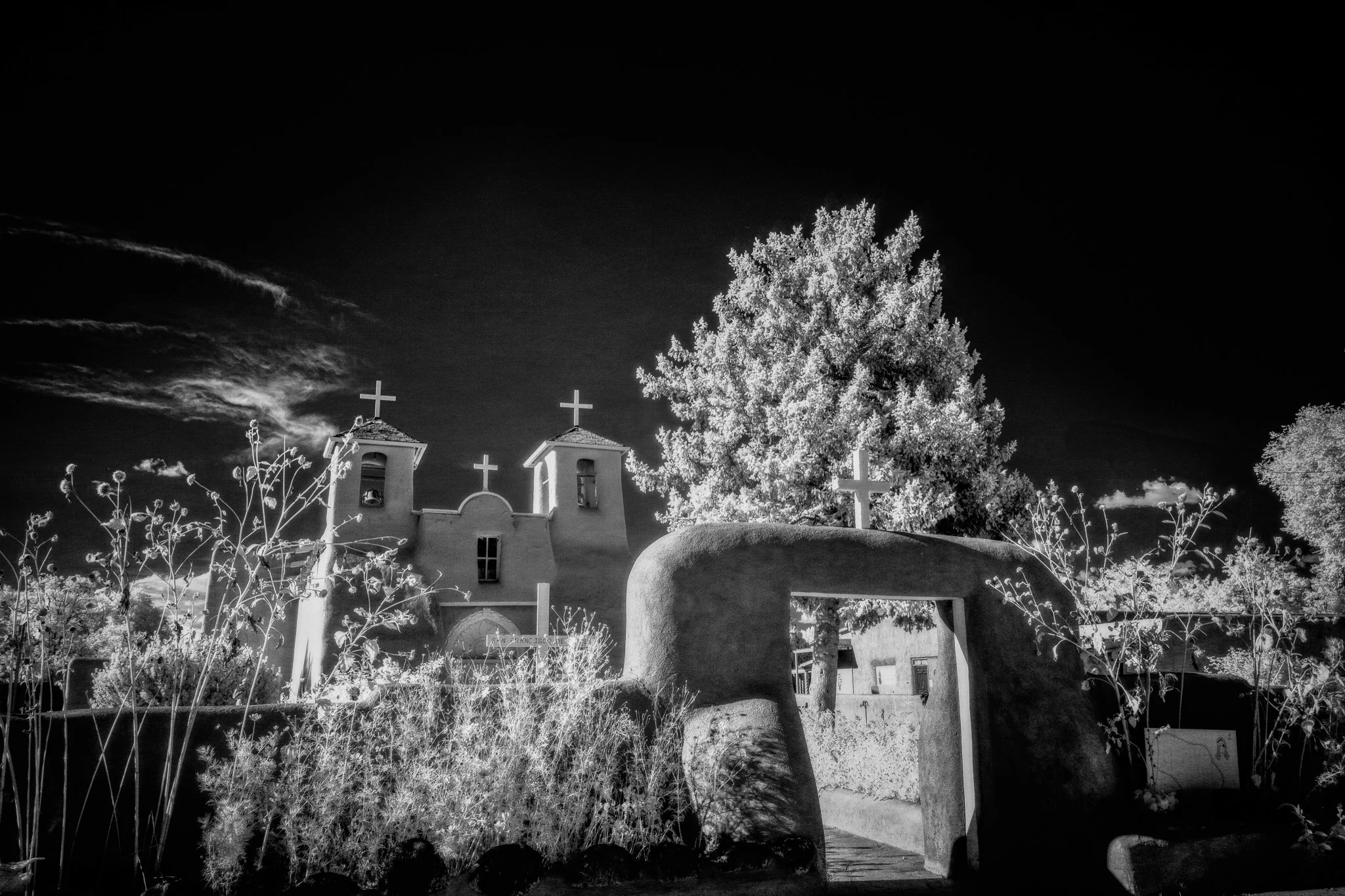 Historic San Francisco de Asís Mission Church in Taos, New Mexico, framed by an adobe archway in a black and white invisible light photograph.