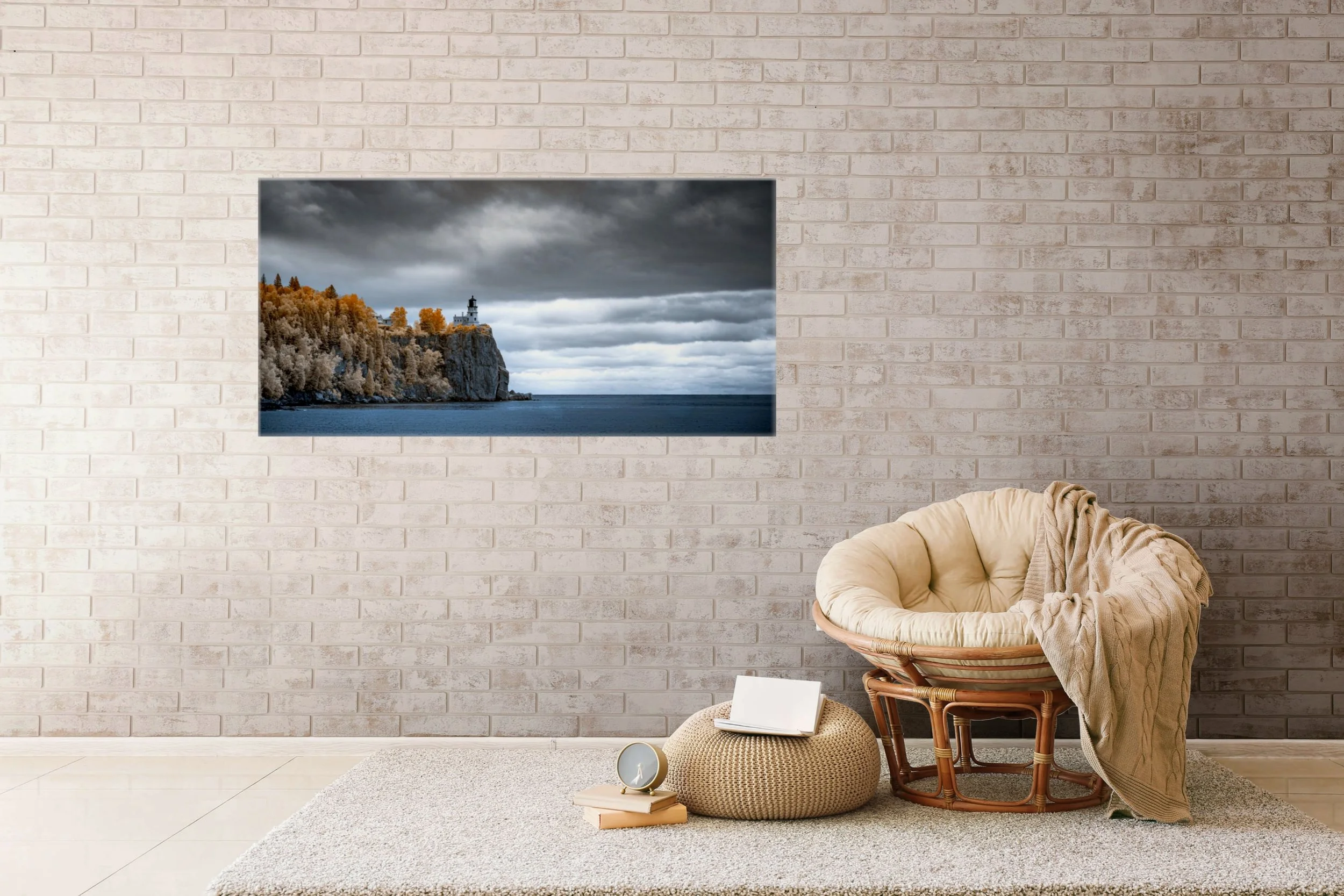 Golden Sentinel at Split Rock landscape photograph displayed on a pale brick wall above a cozy chair, showing Split Rock Lighthouse above Lake Superior beneath a dramatic cloudy sky.