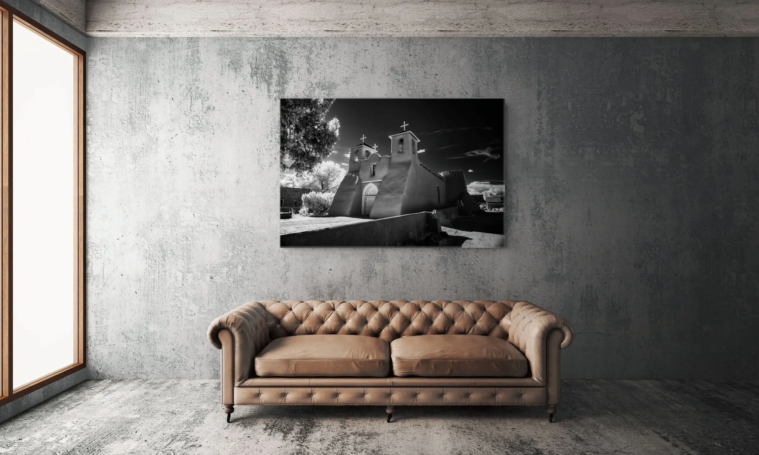 Black-and-white infrared photograph Sanctuary of Timeless Shadows displayed above a brown leather sofa in a contemporary room with textured gray walls.
