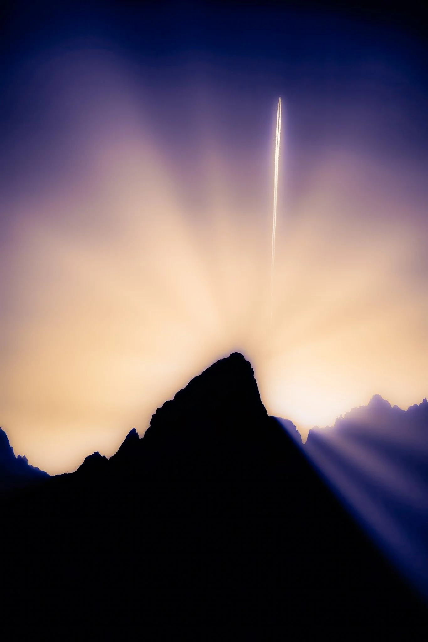 A mountain silhouette at night with a bright launch rocket streaking upward and rays of light emanating from behind the mountains.