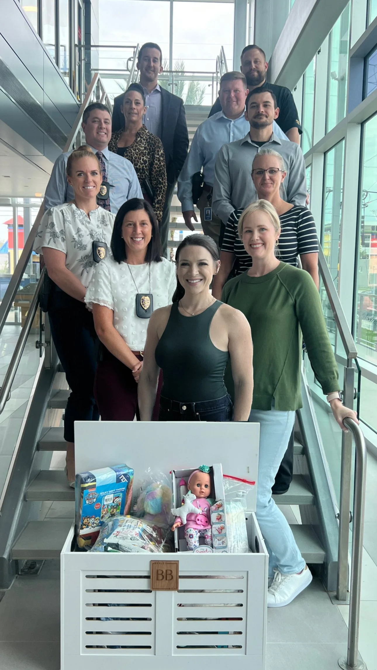 A group of people standing on a staircase inside a modern building, with a toy collection and a doll in a box at the front.