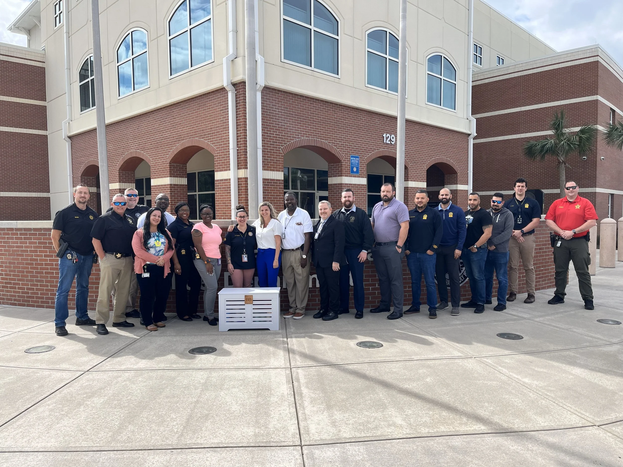 Group of people standing outside a brick building, some wearing uniforms with badges, posing for a photo.