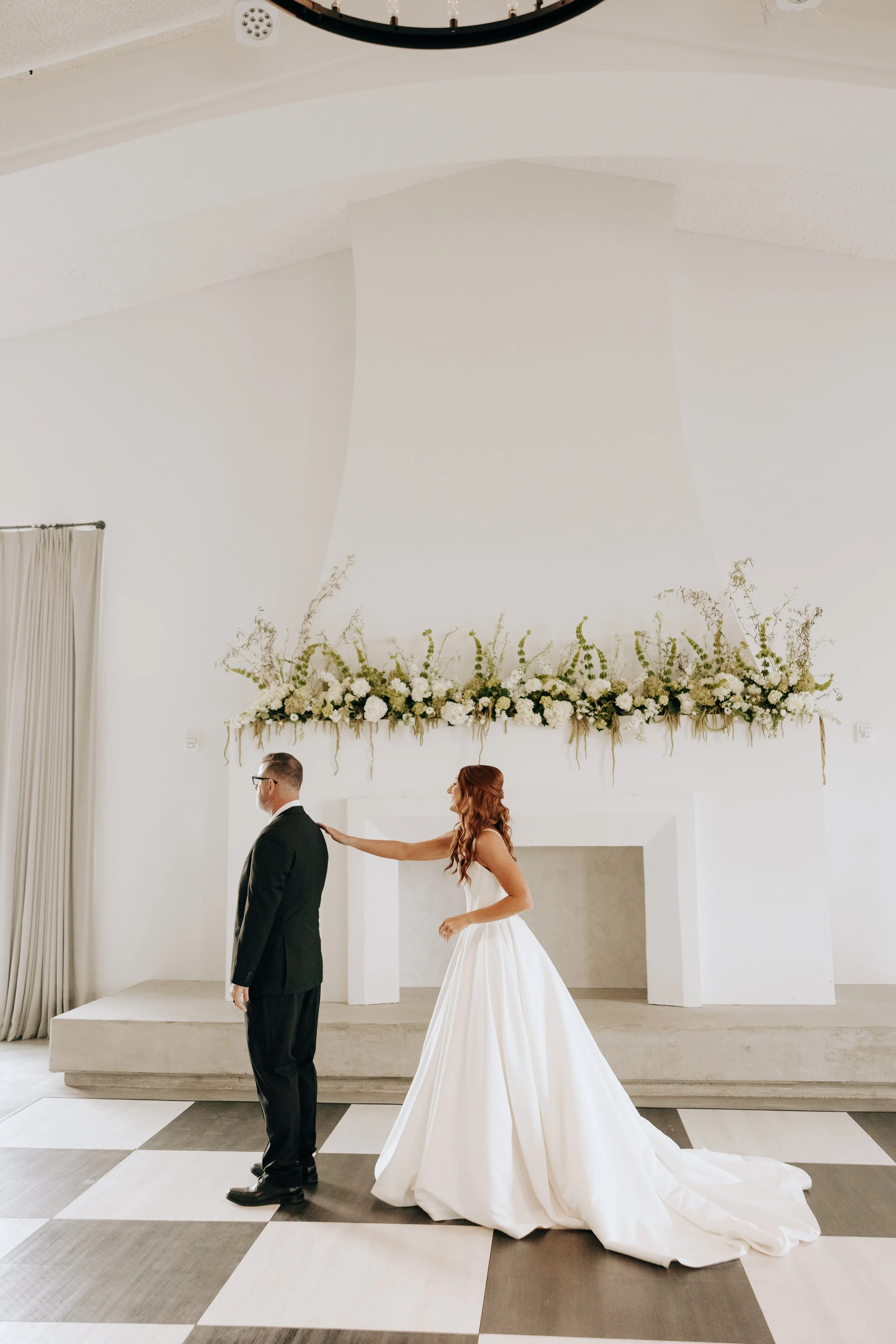Bride touching groom's shoulder during wedding ceremony in a white decorated room.
