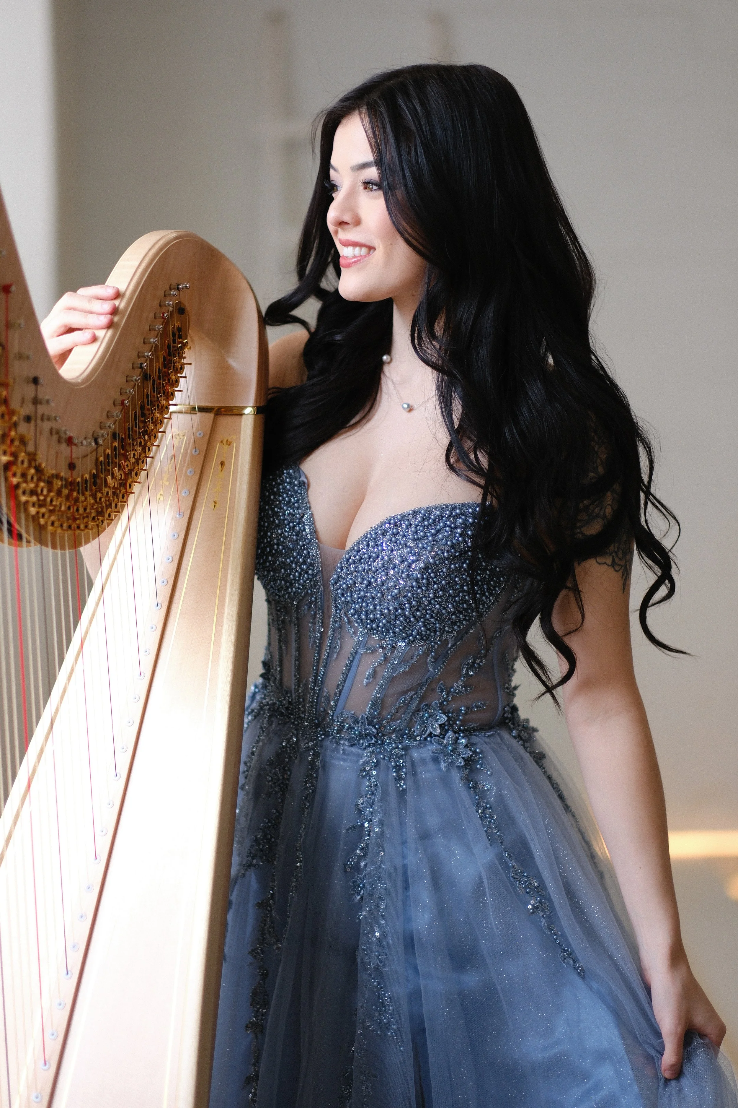 A woman with long black hair wearing a sparkly blue gown playing a harp.