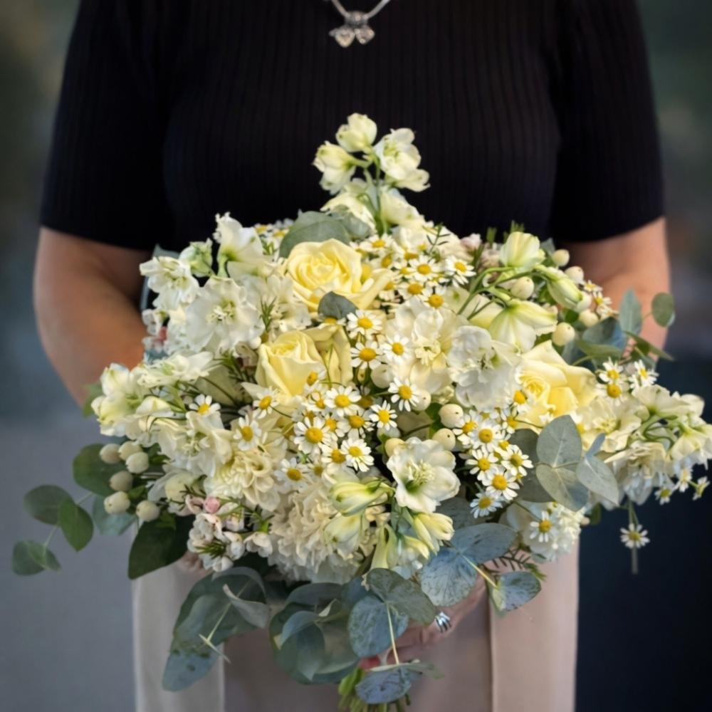 Florist holding a hand-tied bouquet of white and yellow flowers