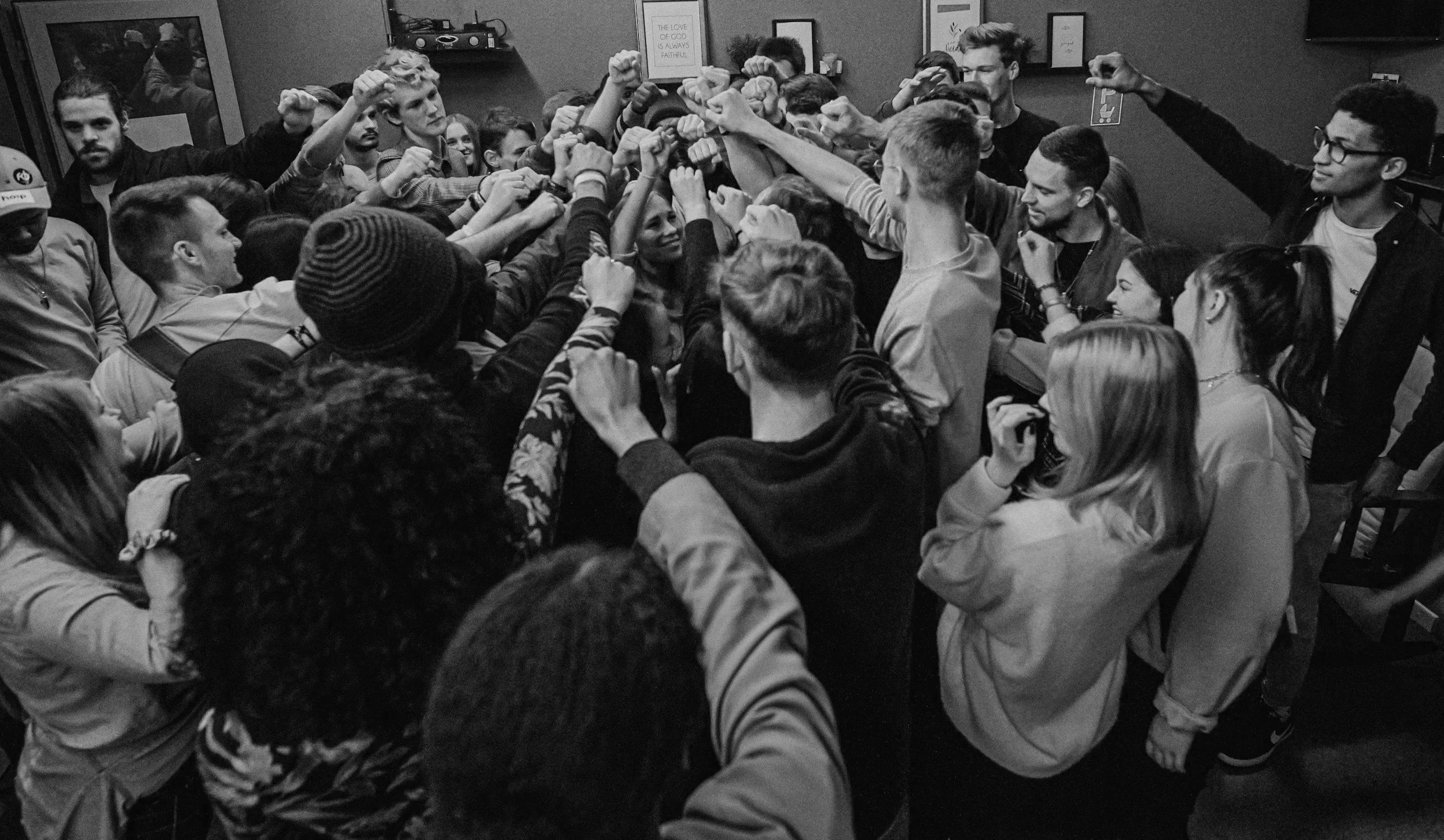A large group of young people gathered in a room, raising their fists and hands together in a show of solidarity or celebration.