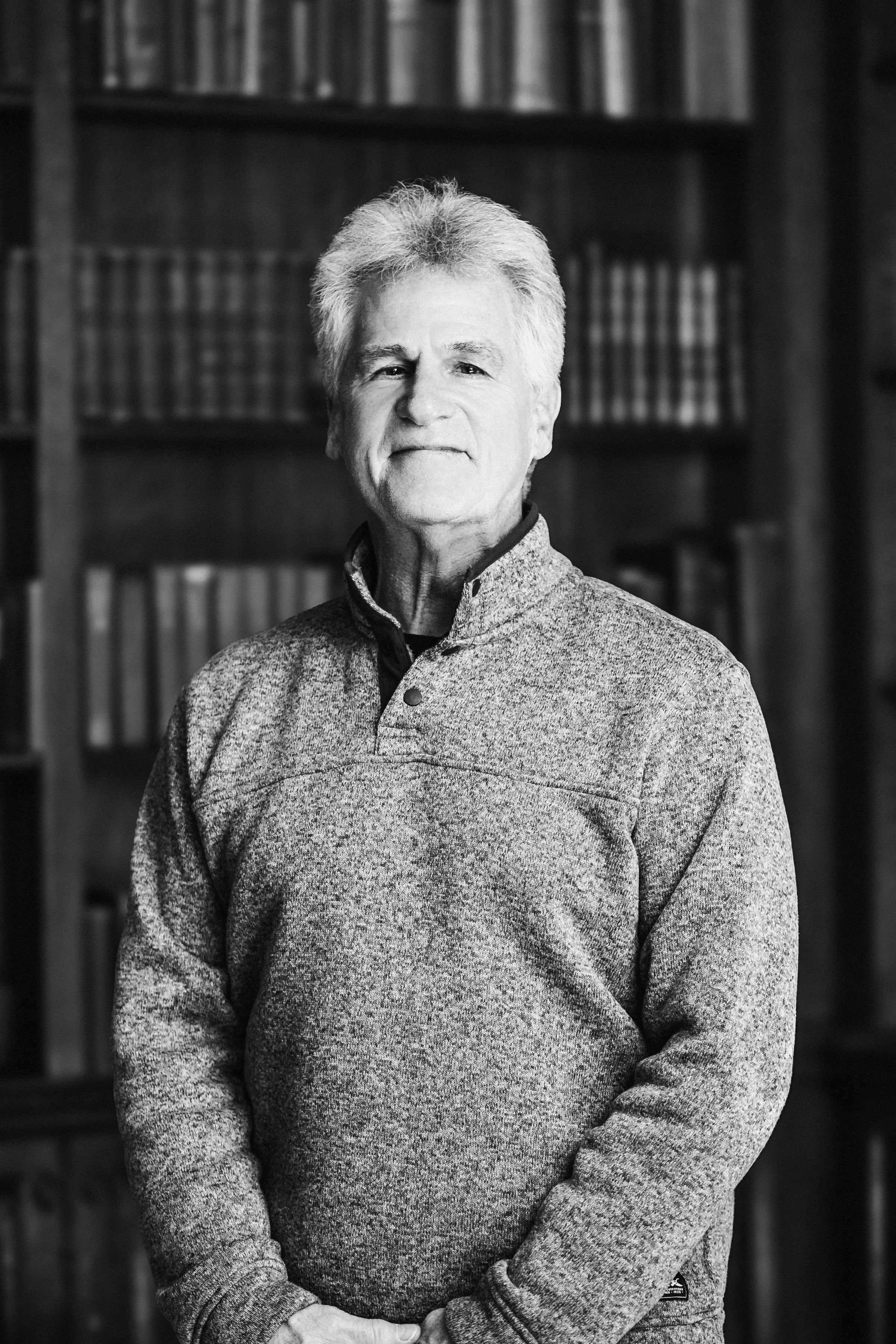 A black-and-white photo of a middle-aged woman with short hair, smiling slightly, standing in front of a decorative light background.