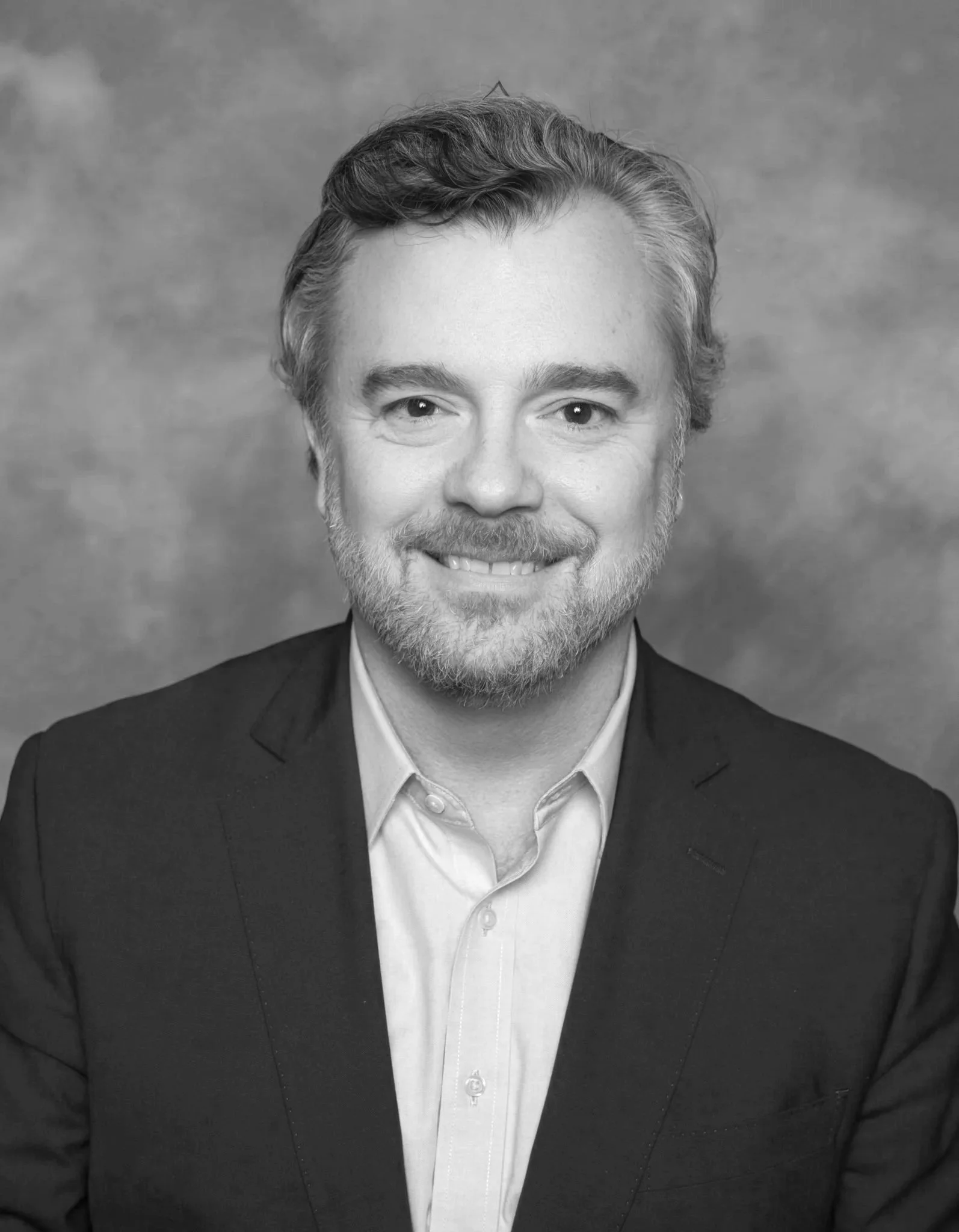 Professional portrait of a man in a suit standing in front of American and state flags.
