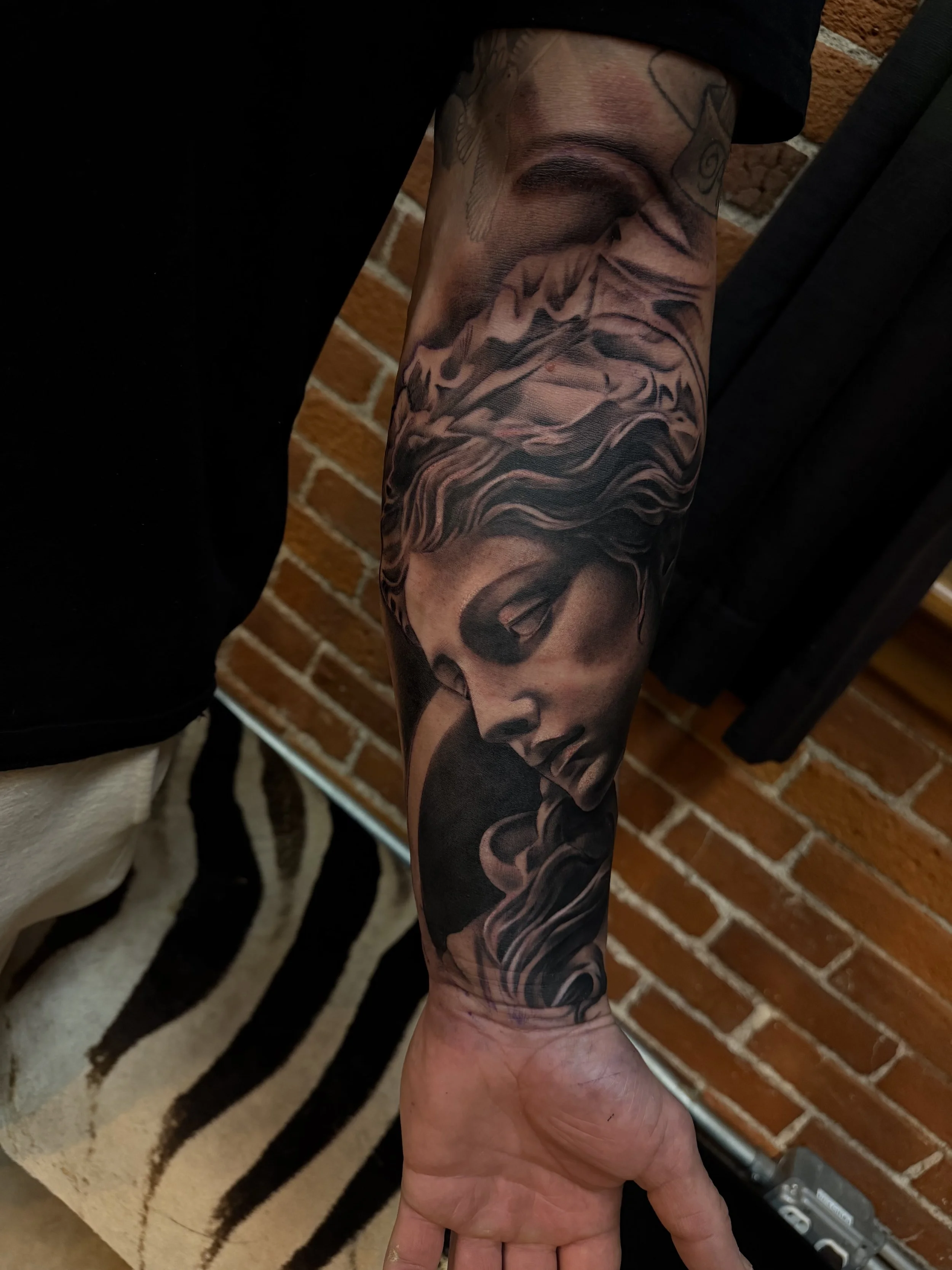 Black and gray tattoo of a woman with flowing hair, holding a skull, on a person's forearm.