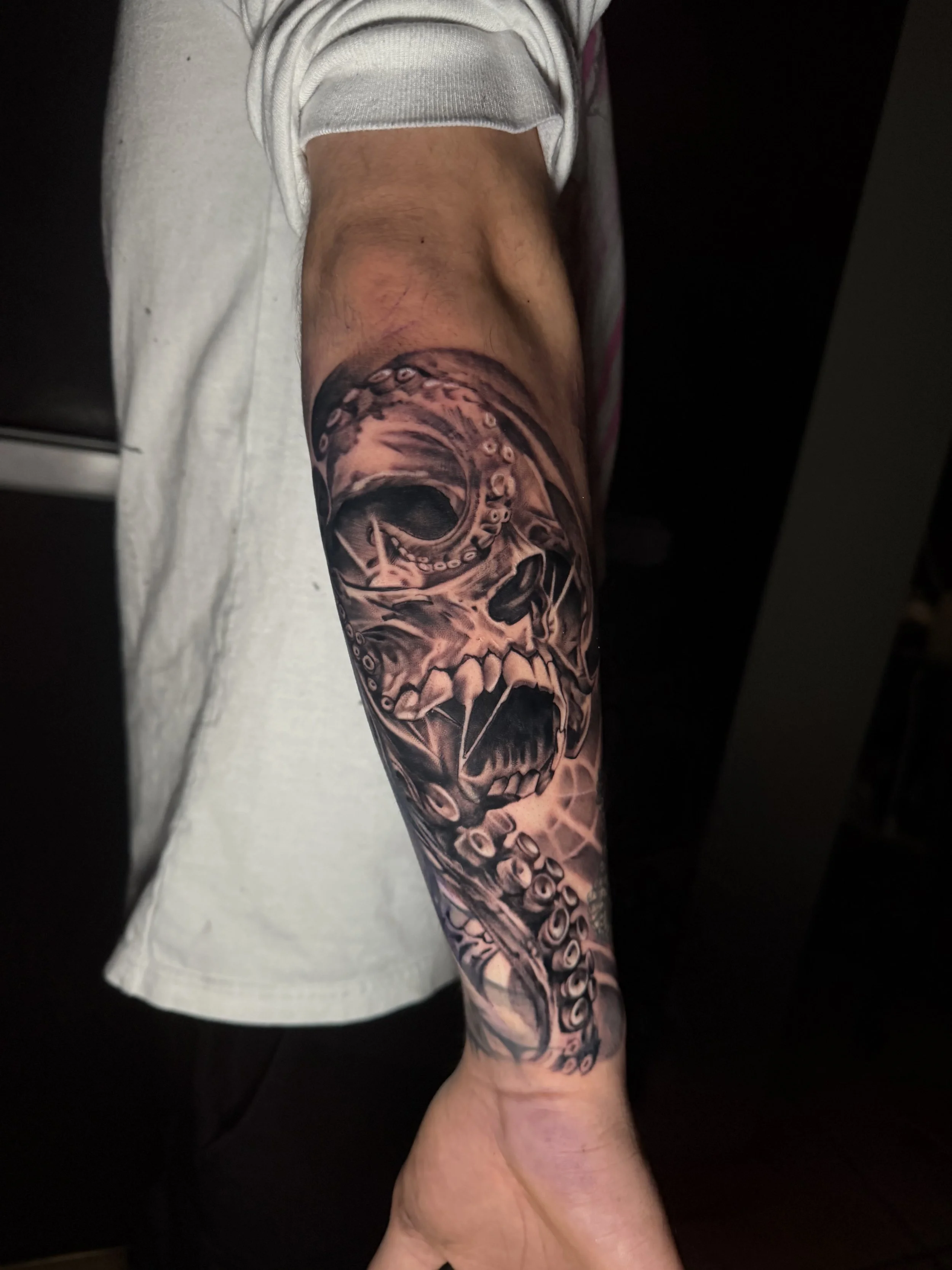 Black and gray tattoo of a skull and octopus on person's arm.