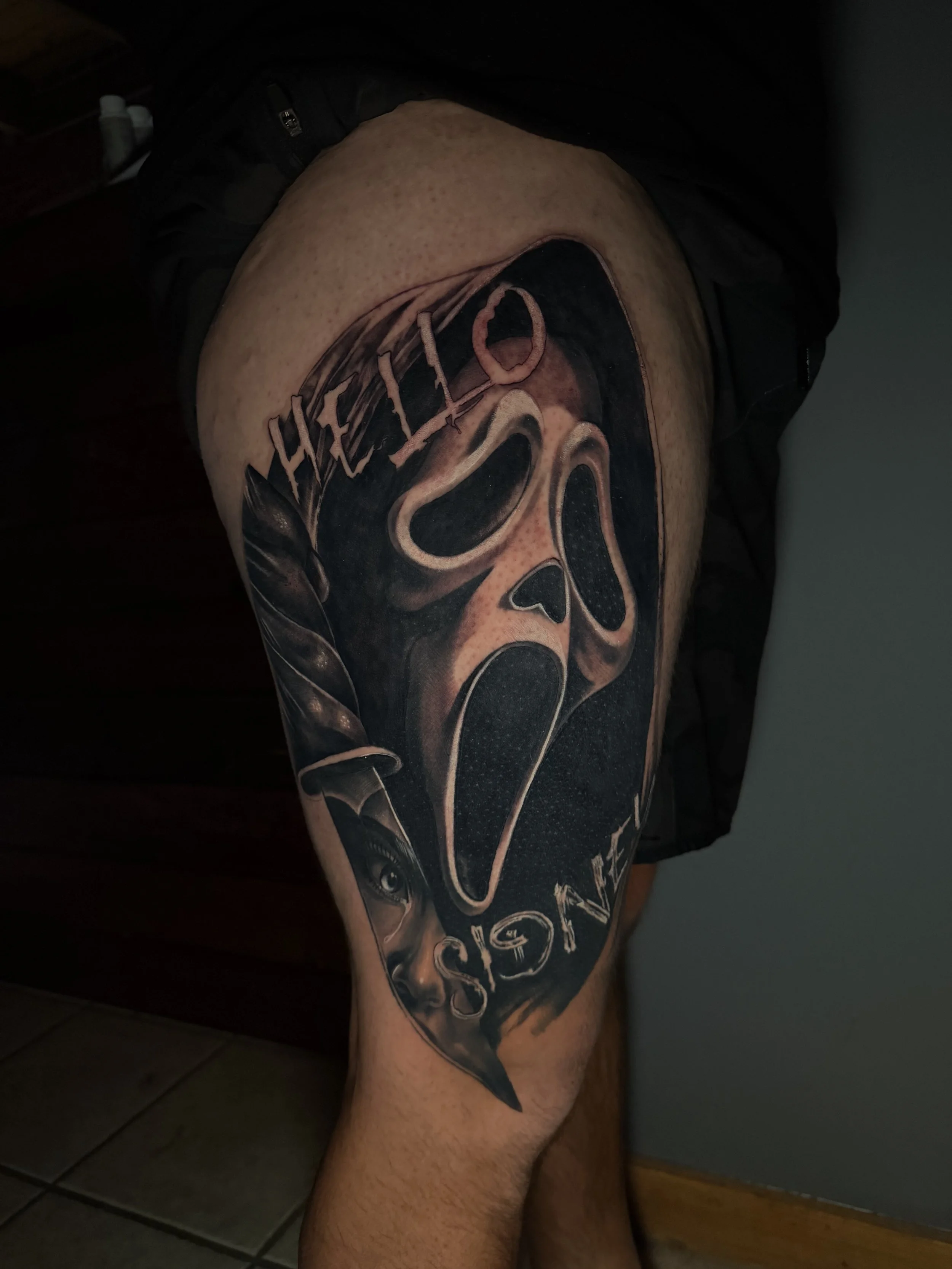Tattoo of a ghost face mask from the movie Scream, with the word 'HELP' above and 'SISTERS' below, on a person's thigh.