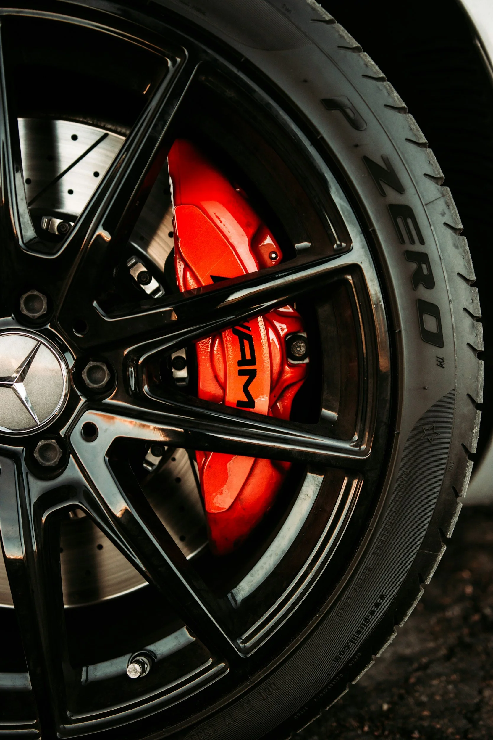 Close-up of a car wheel featuring a black alloy rim, a red brake caliper with AMG branding, and a tire with visible tread.