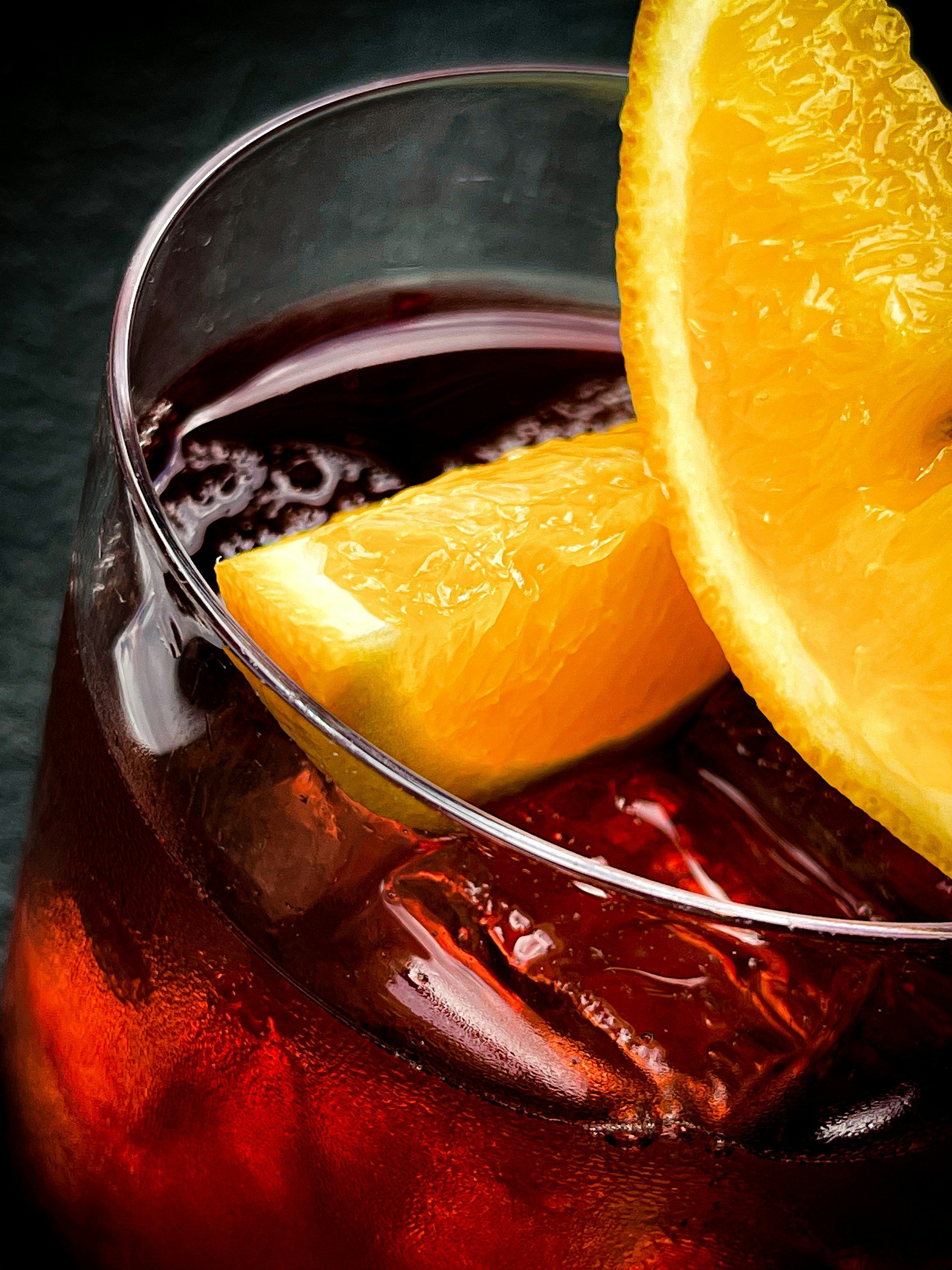 Close-up of a glass of dark red beverage with ice and two orange wedges as garnish.