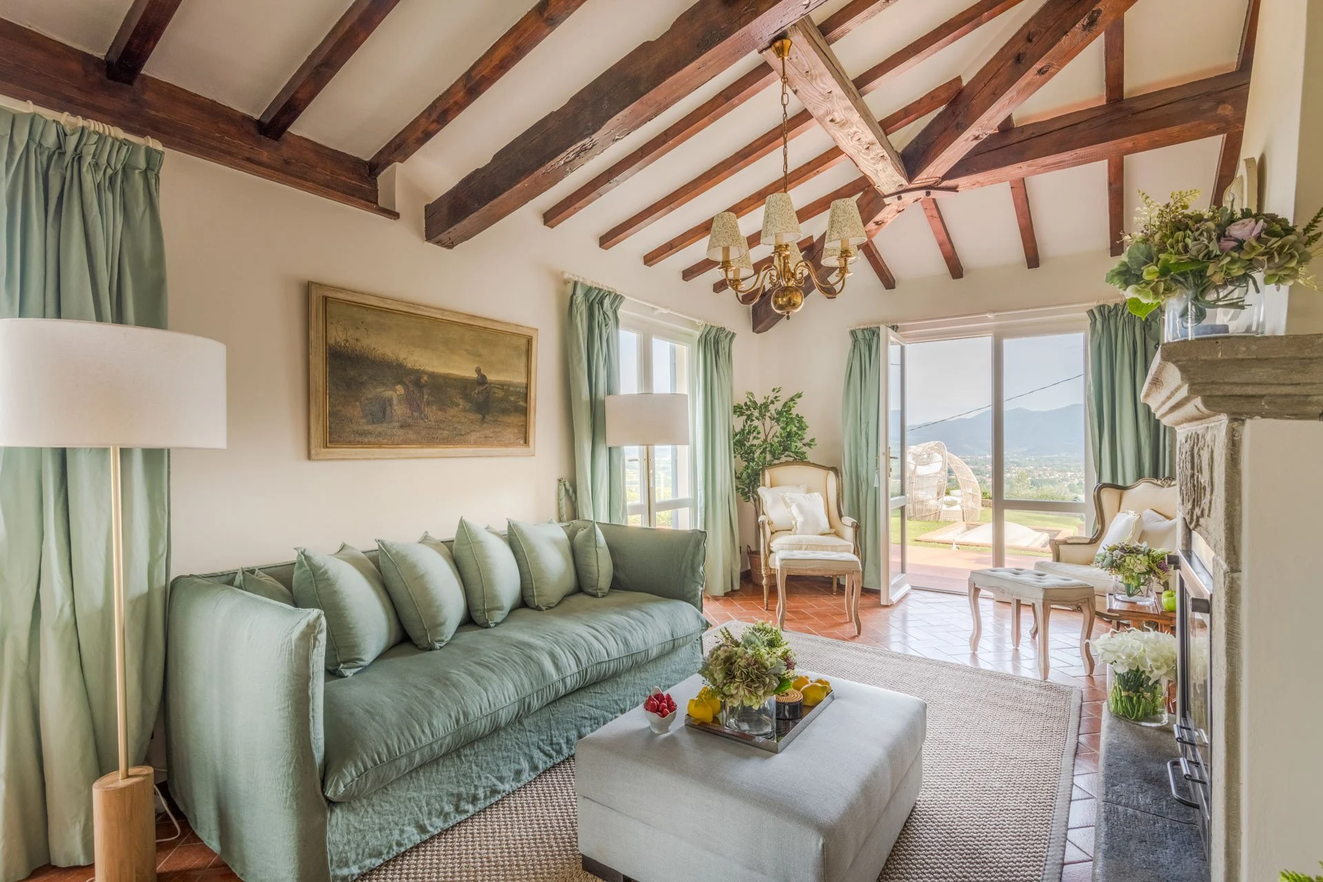 Living room with green sofa, armchair, chandelier, and large windows offering mountain view.