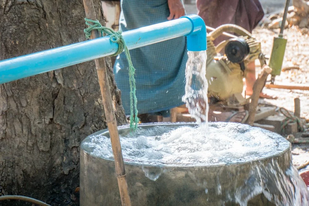Water flowing from a newly drilled well in a rural village in myanmar, with a person in the background.