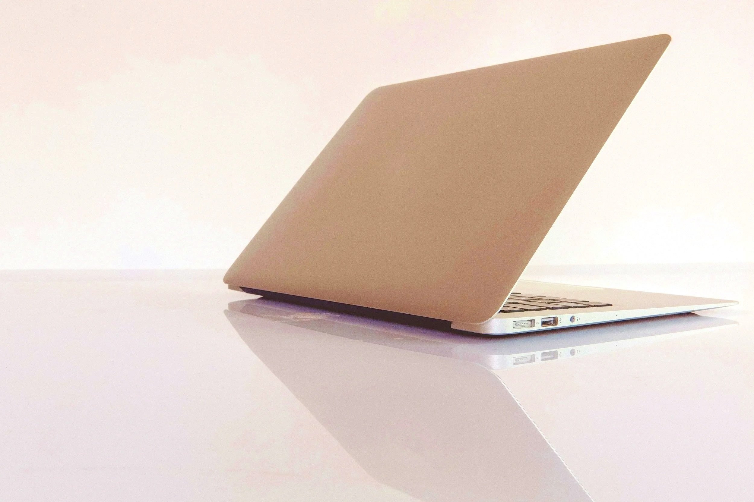 Silver laptop with a closed beige cover on a reflective white surface.