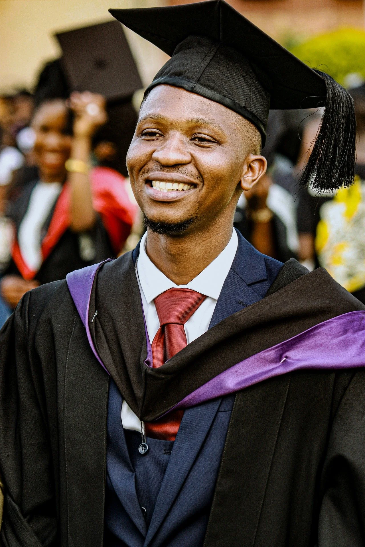 A proud young man in a graduation gown and cap, smiling at his graduation ceremony.