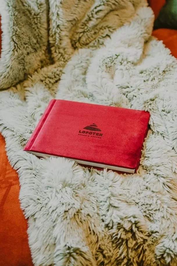 A red hardcover book titled 'LOFOTEN' rests on a fluffy beige blanket.