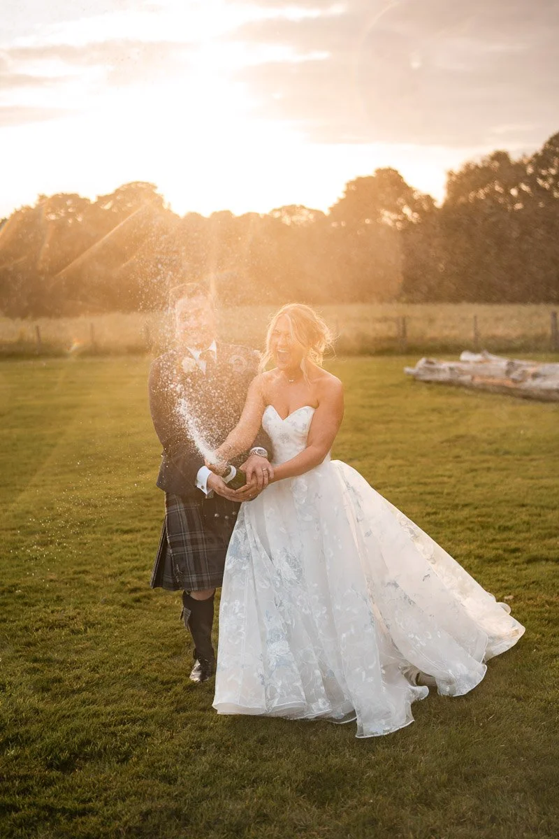 Bride and groom celebrating wedding outdoors at Cornhill Castle, with golden hour sunlight shining through, champagne spraying, and joyful expressions.