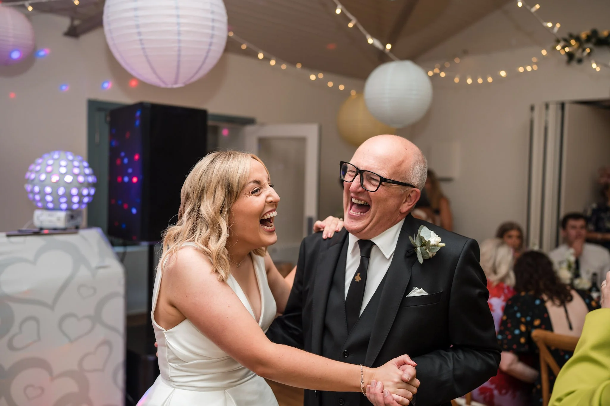 A bride and her dad dancing and laughing at a wedding reception.