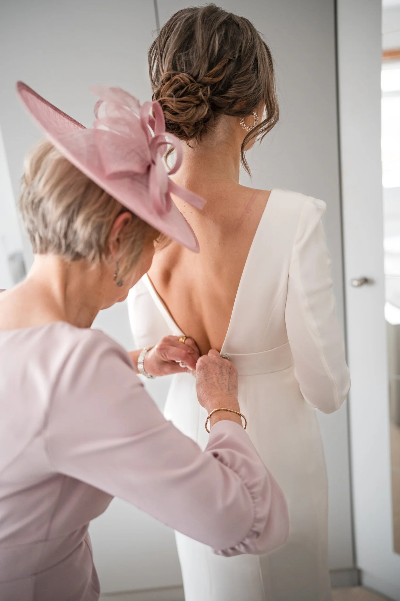 An mother of the bride helps her daughter button her white wedding dress.