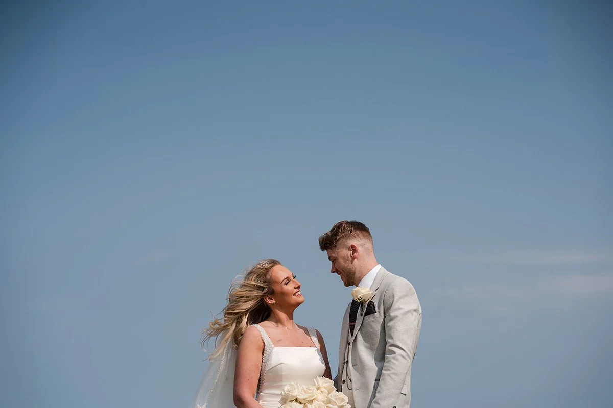 Bride and groom smiling at each other during relaxed outdoor wedding portraits against a clear blue sky in Scotland