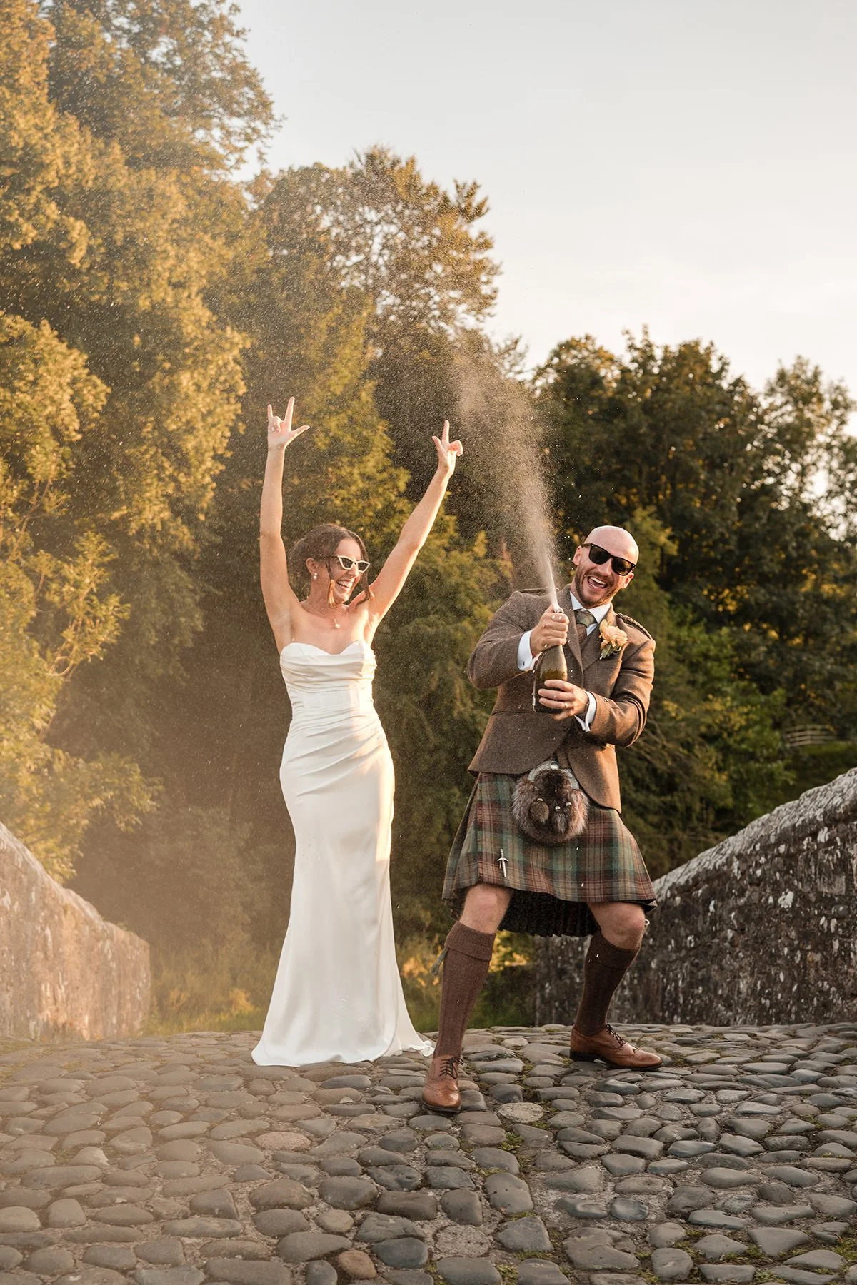 Bride and groom spraying champagne on Brig o’ Doon bridge at sunset in Ayrshire