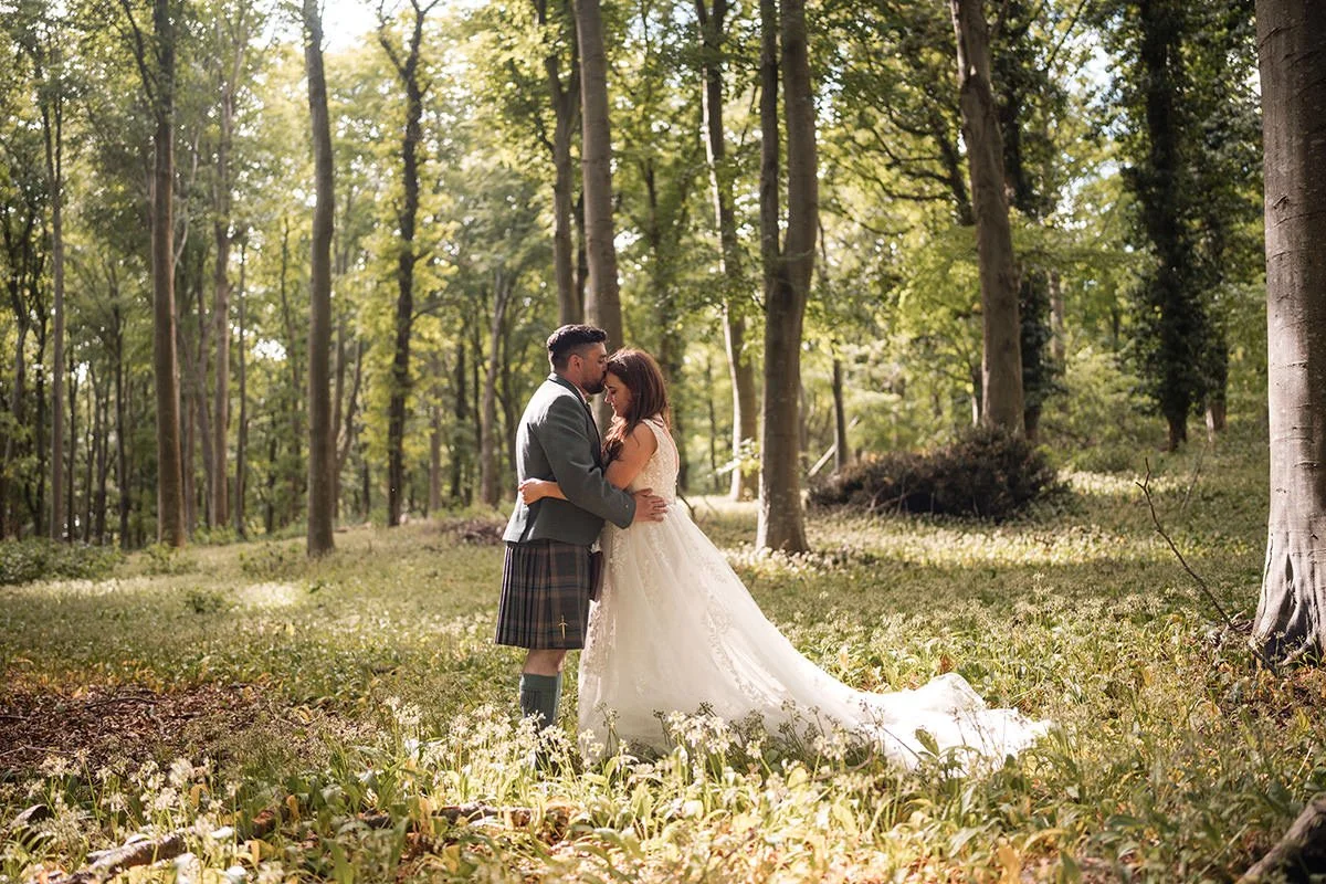 Bride and groom embracing during a romantic woodland wedding portrait at Broxmouth Courtyard in East Lothian, photographed by a Scottish wedding photographer