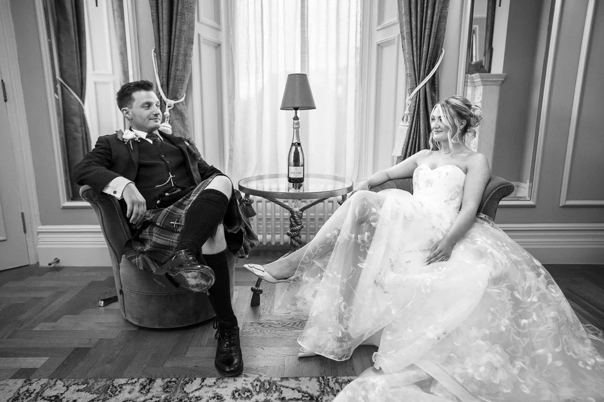 A bride and groom in wedding attire sitting in a room with elegant decor at their wedding at Cornhill Castle