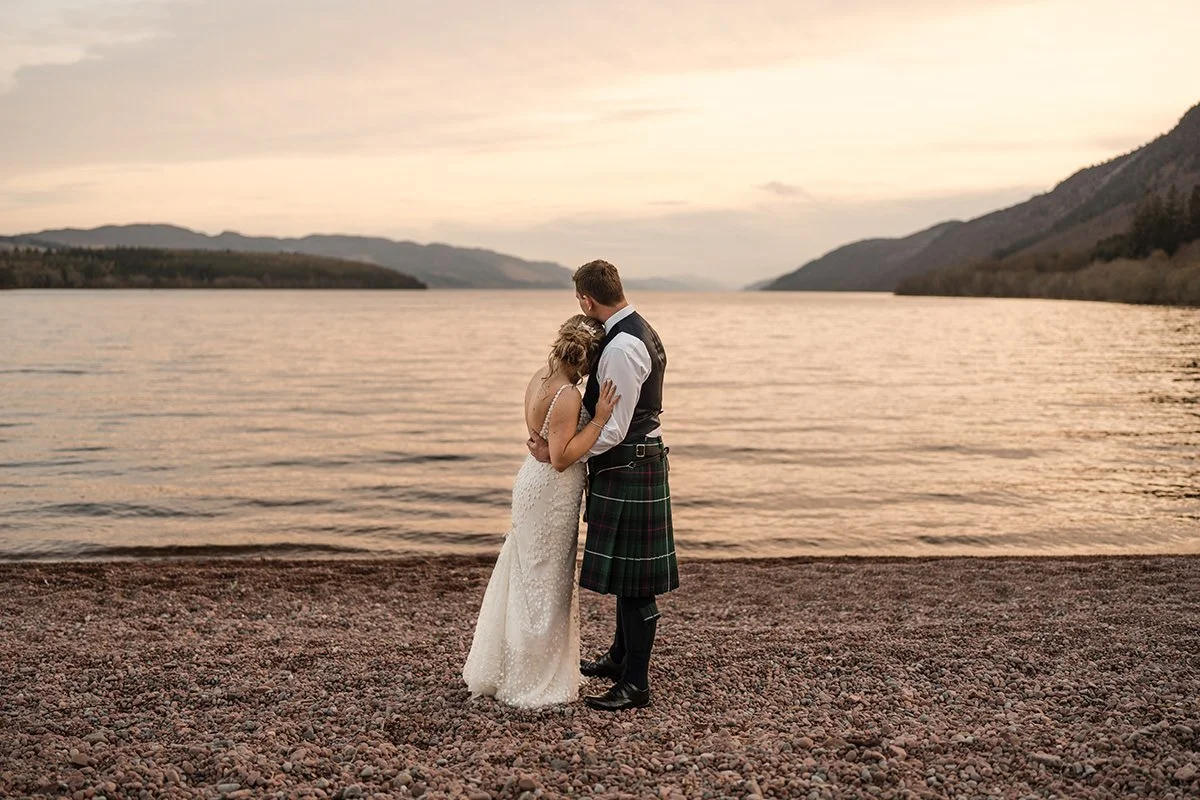 Bride and groom embracing on the shore of Loch Ness at sunset during a romantic wedding portrait session
