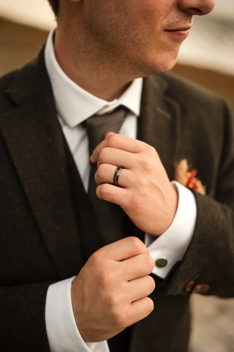 Close-up of a man adjusting his tie, wearing a dark suit and a wedding band on his left hand at an elopement in Dunoon