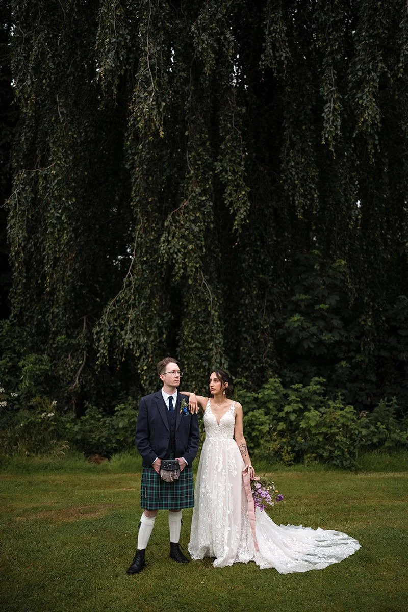 Bride and groom standing together beneath trees at Restoration Yard in Dalkeith during a relaxed outdoor wedding.
