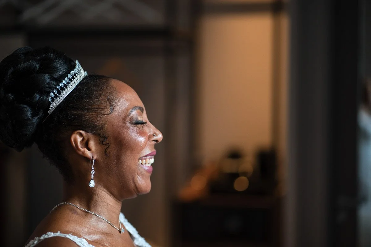 A woman in a wedding dress smiling with her eyes closed, wearing a tiara, earrings, and a necklace, with a blurred background at their Glasgow City Elopement
