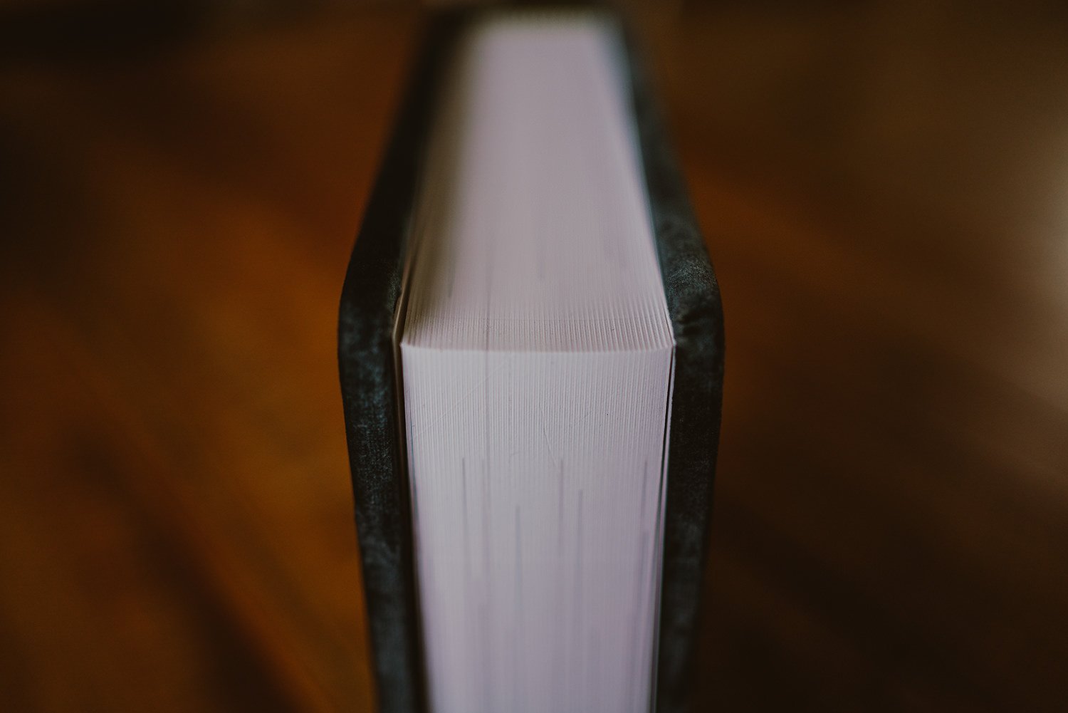 Close-up of a thick book with a black cover on a wooden surface, focusing on the top edge of the pages.
