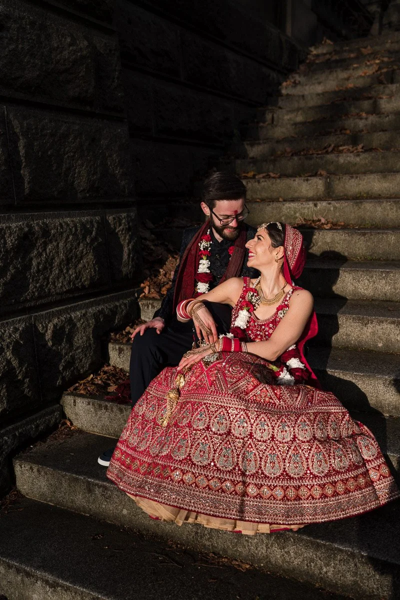 A bride and groom sitting on outdoor stone steps at night, dressed in traditional wedding attire, smiling at each other in Glasgow West End
