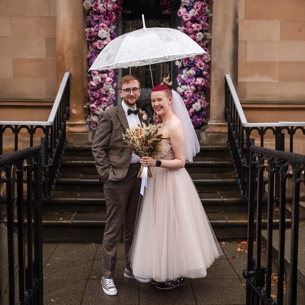 Wedding couple standing together under a clear umbrella outside a city centre venue in Glasgow