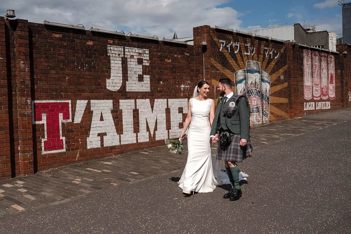 Glasgow elopement couple walking past the Tennent’s Wellpark Brewery mural in Dennistoun.