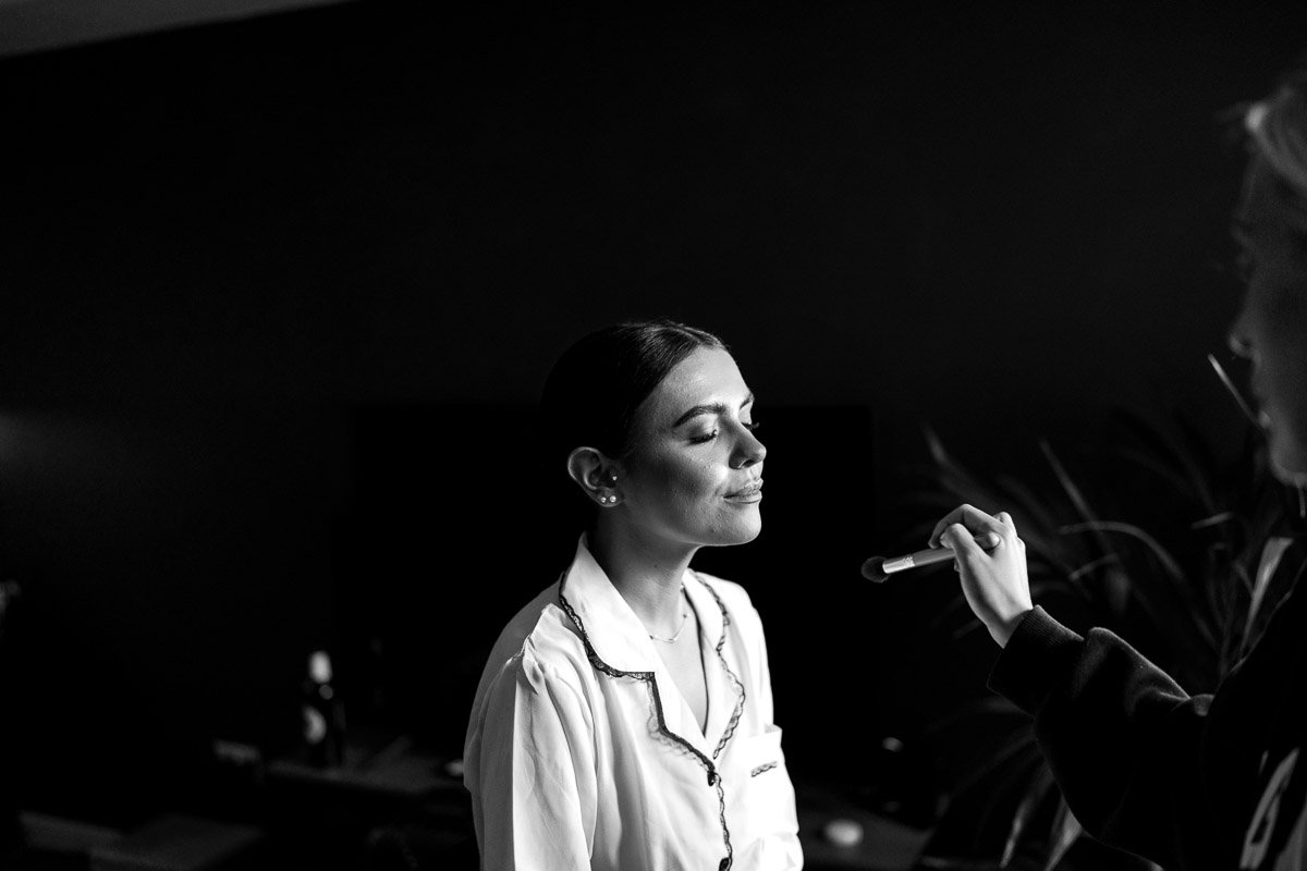 A woman in pajamas getting her makeup applied by another person.