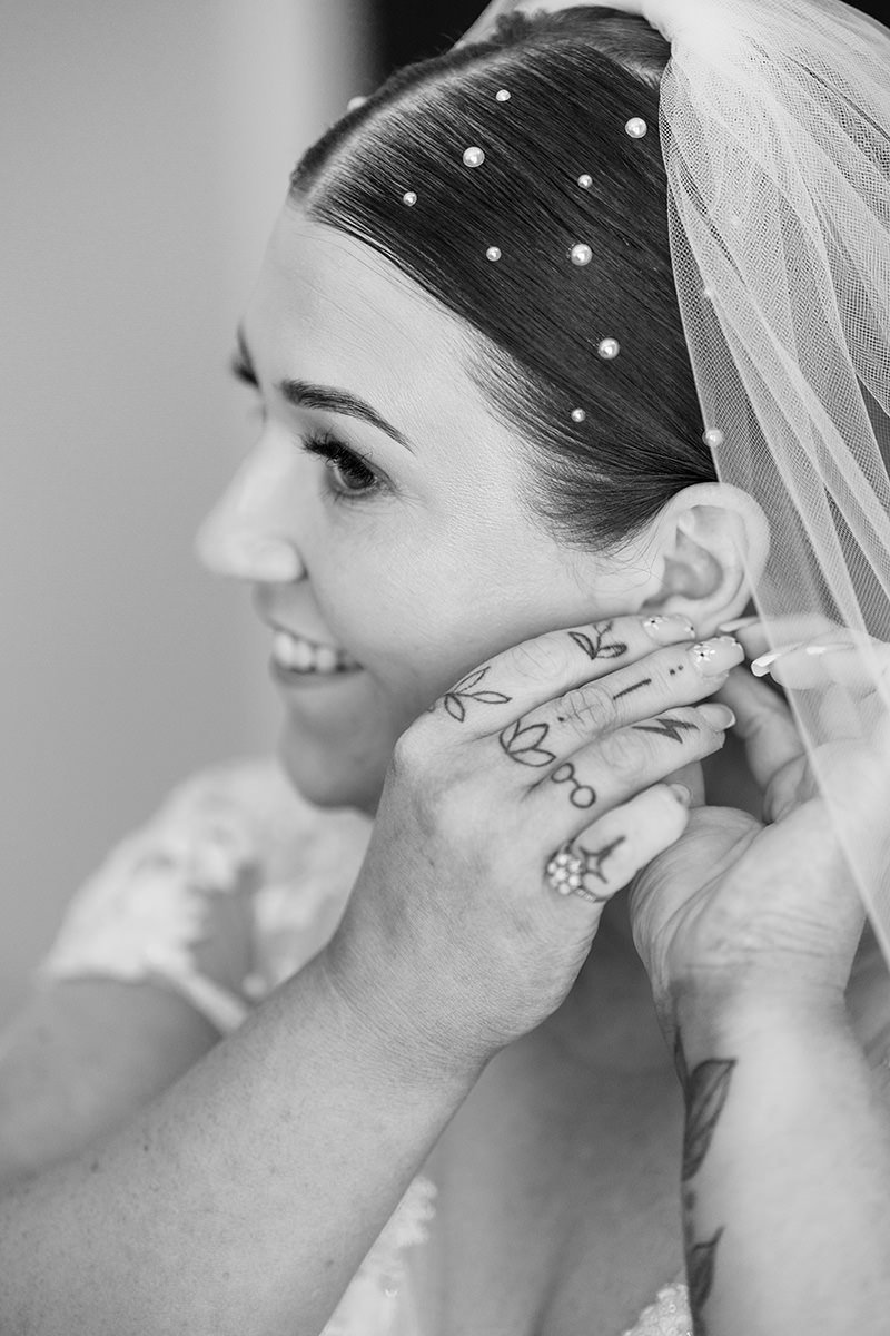 Bride smiling as she puts on her earrings during bridal prep, black and white portrait