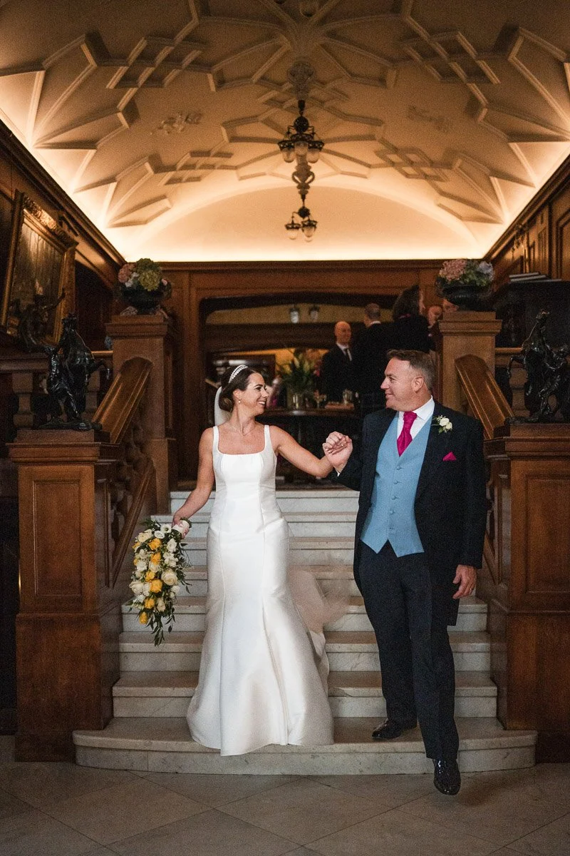 Bride and groom dancing on staircase inside a decorated venue, with guests in background at Sorn Castle