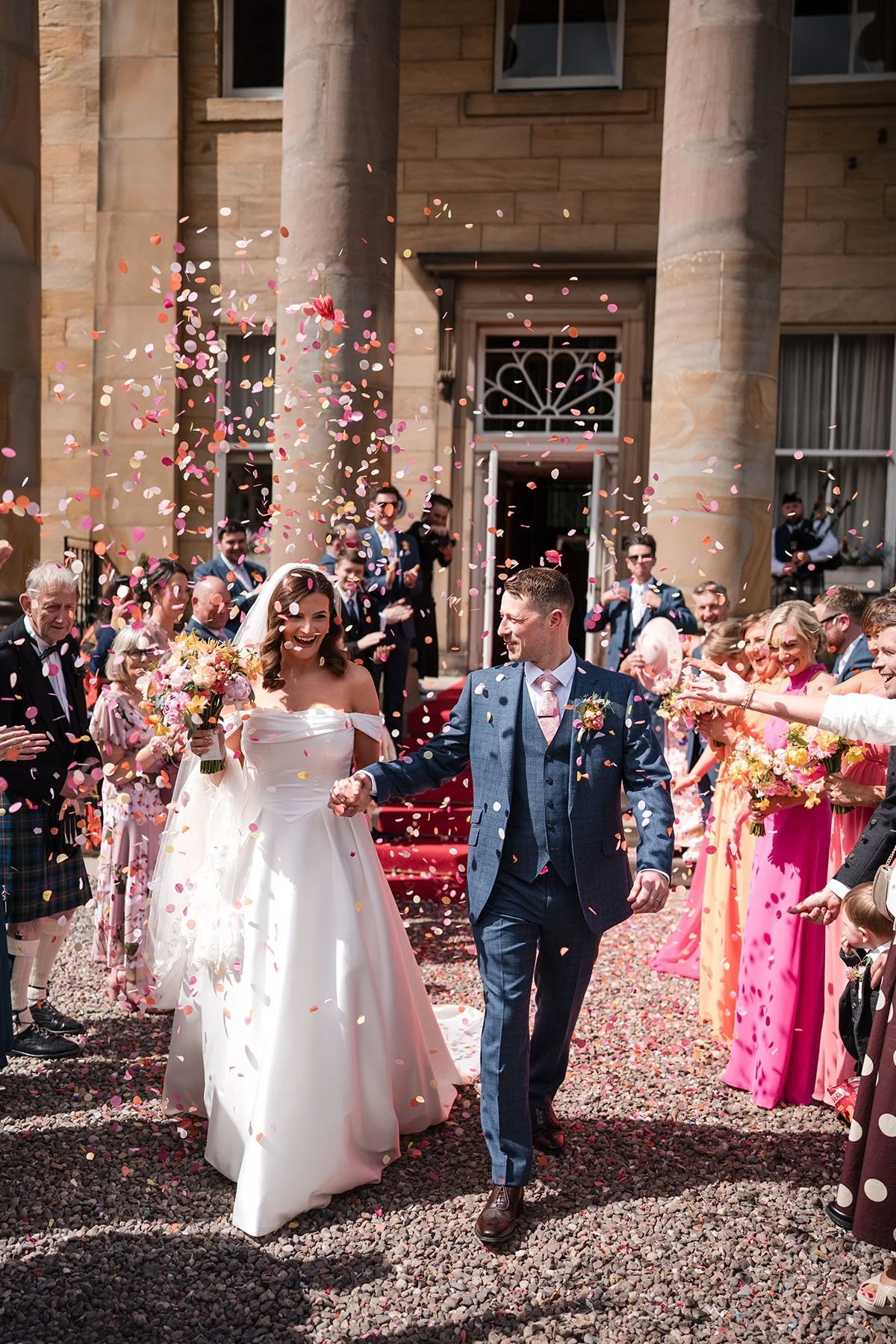 Bride and groom walking through colourful confetti outside Balbirnie House Hotel in Scotland