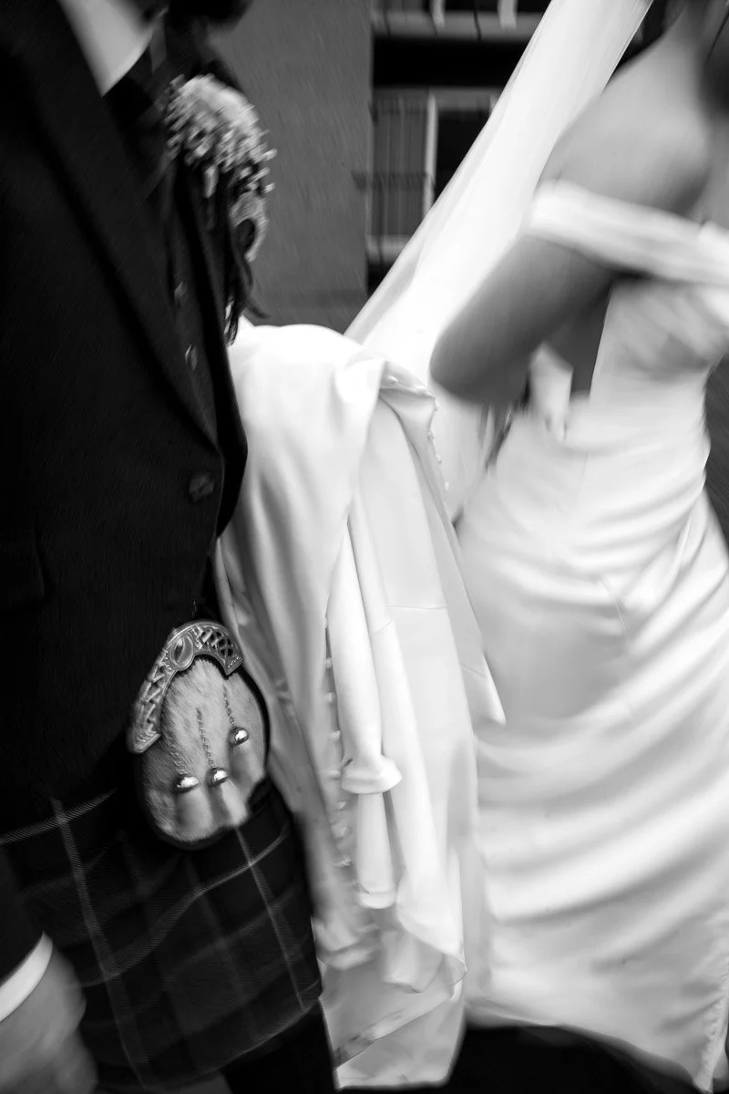 Close-up of a person in a groom in a kilt standing next to a bride in a wedding dress.