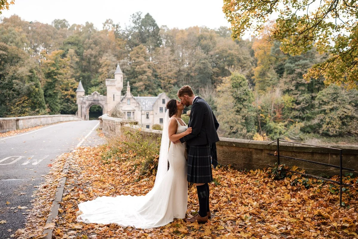 A bride and groom sharing a kiss at Mauldslie Bridge, Lanarkshire, after their Radstone wedding during Autmn on a fallen-leaf-covered bridge.