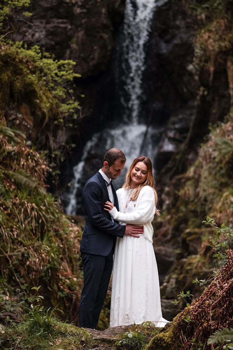 Couple embracing in front of a waterfall during their Aberfoyle elopement in Scotland, photographed by Scottish elopement and wedding photographer Andy Hamilton.