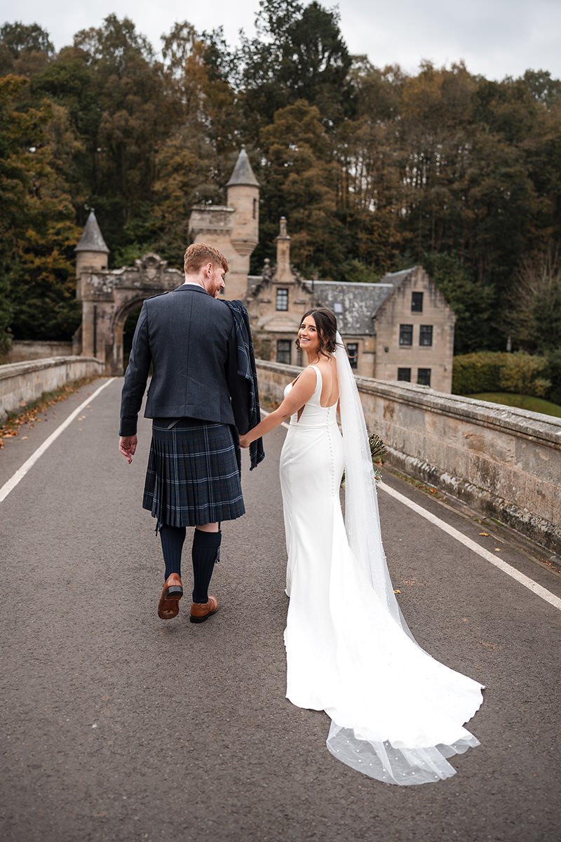 Wedding couple walking hand in hand across Mauldslie Bridge in Lanarkshire after their Radstone Hotel wedding