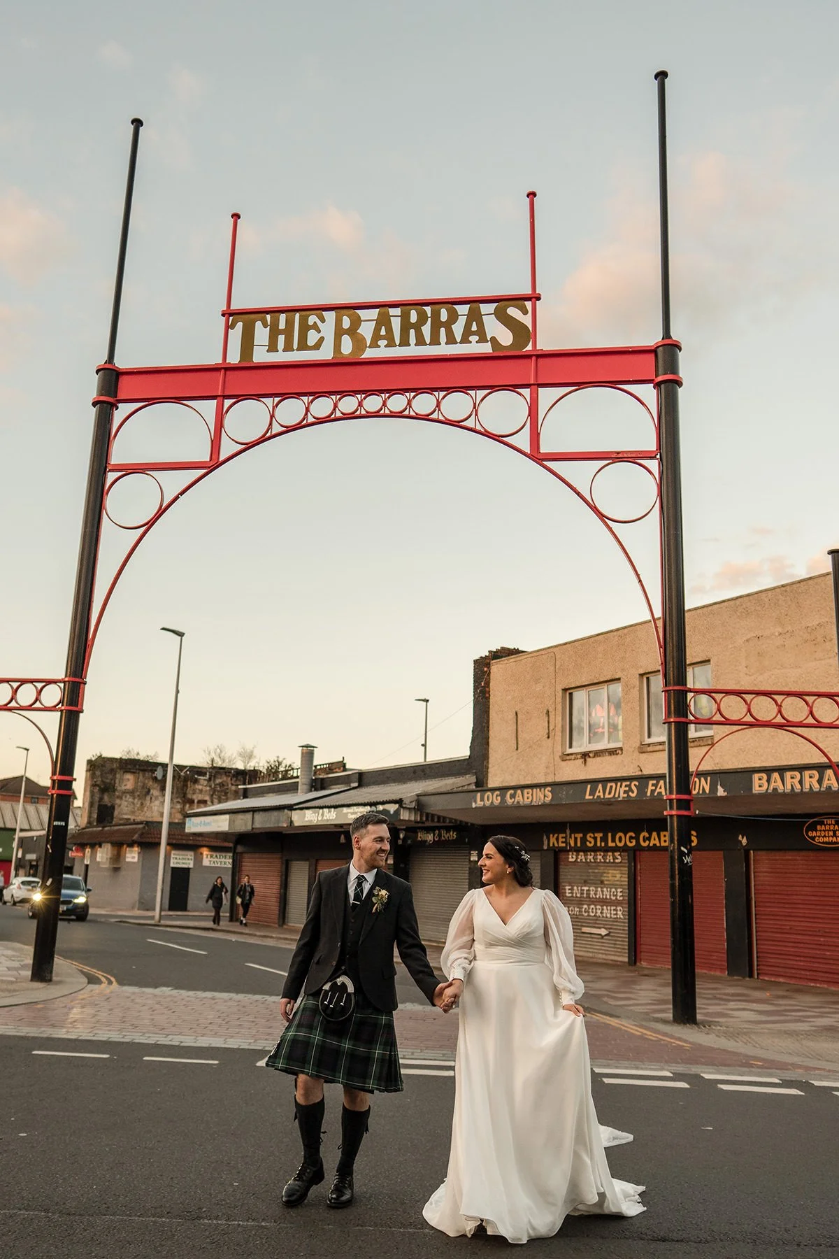 Bride and groom walking hand in hand under The Barras market sign in Glasgow city centre during an urban wedding photoshoot by Glasgow wedding photographer Andy Hamilton.