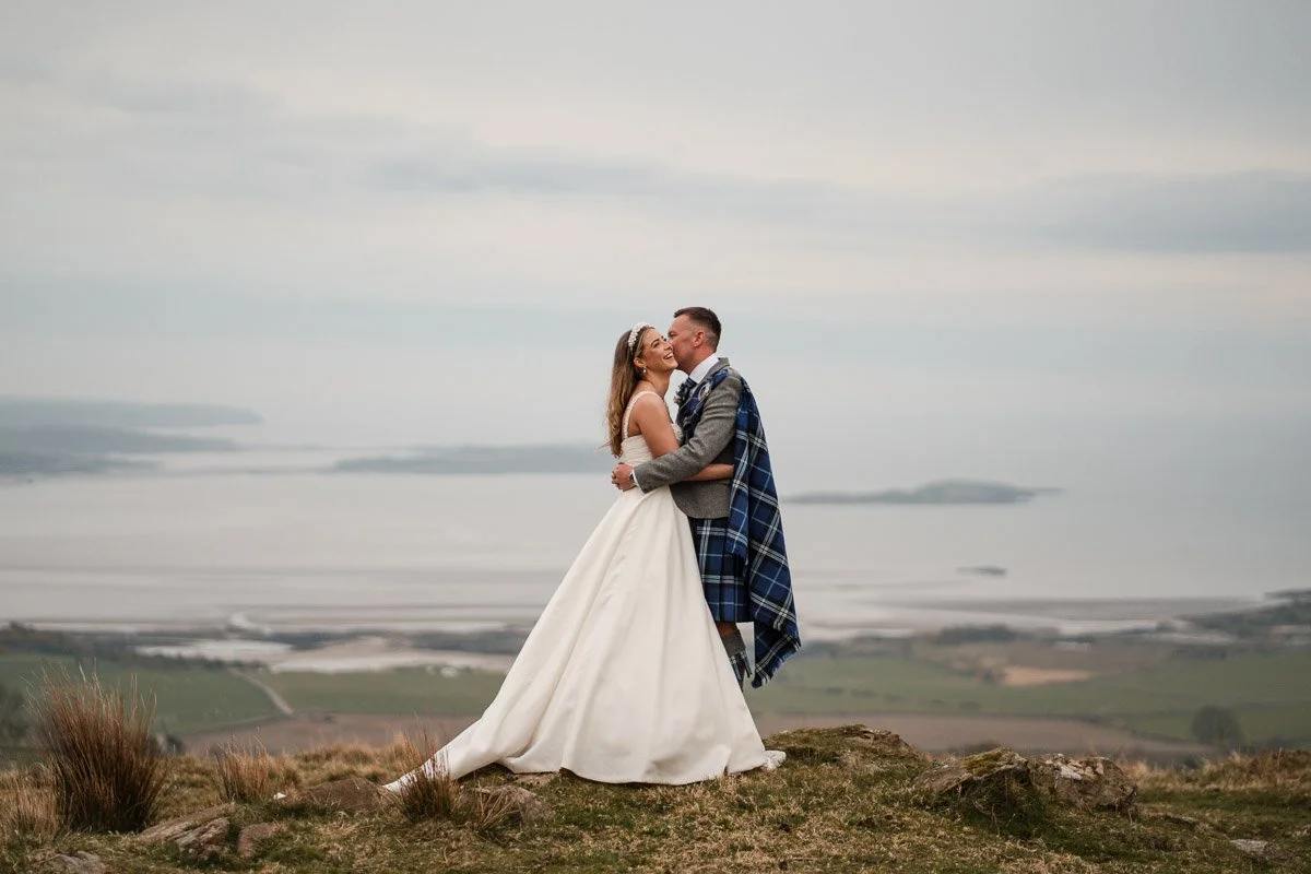 Bride and groom sharing a kiss on a grassy hill overlooking a body of water at GG's Yard