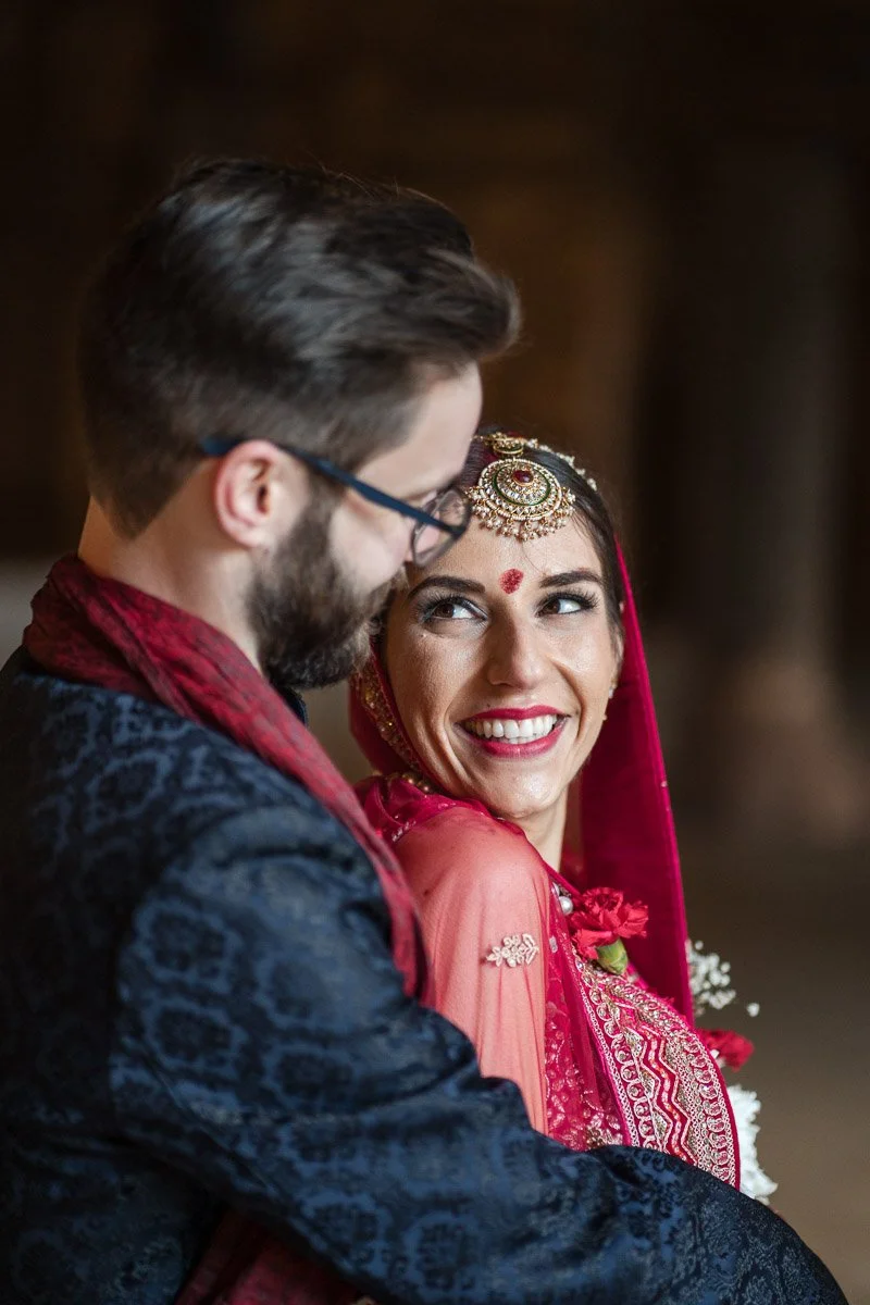A man and woman dressed in traditional Hindu wedding attire in Glasgow, sharing an intimate moment and smiling at each other.