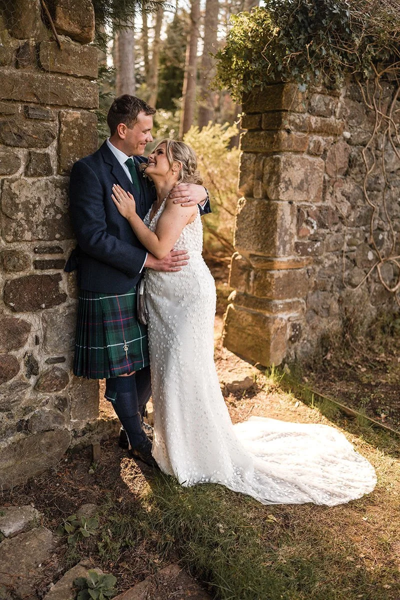 Bride and groom embracing beside stone archways during their wedding at Loch Ness Country House Hotel