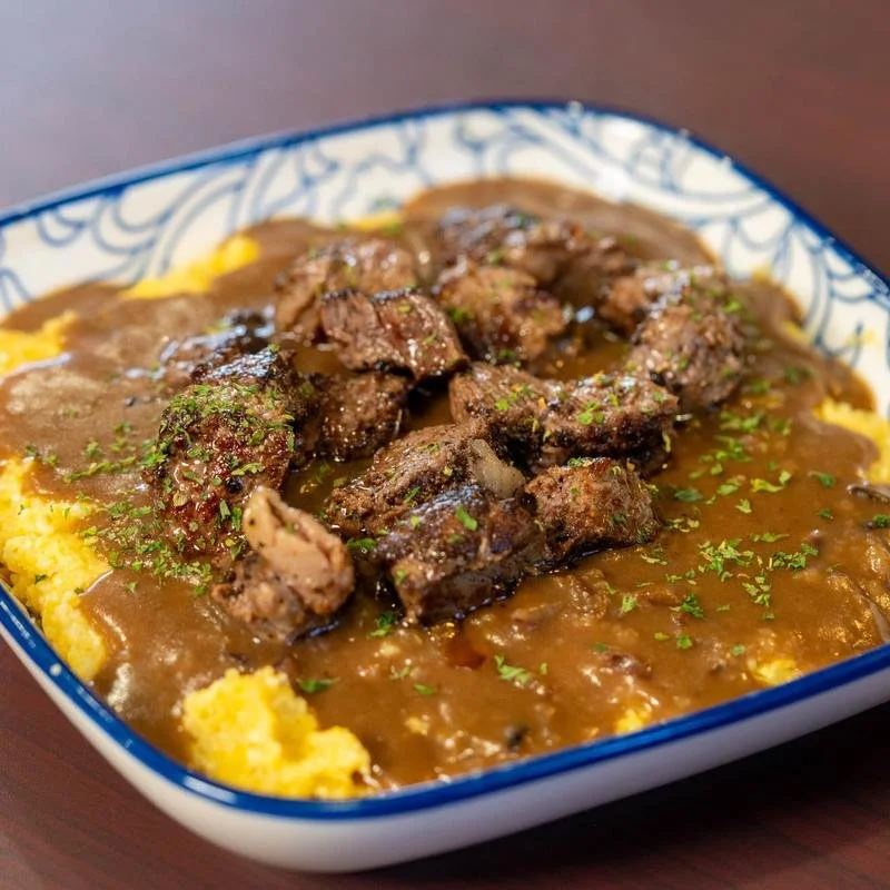 A dish of mashed potatoes topped with meat stew and gravy, garnished with chopped herbs
